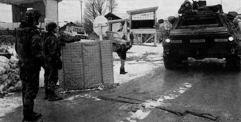 Gate guards look on as a Fox vehicle belonging to the 25th Chemical Company rolls toward the air base's front gate.